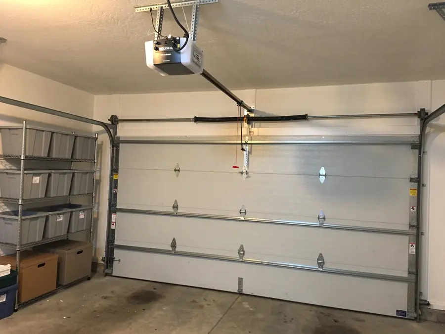 A white garage door is closed with an opener and a torsion spring visible.